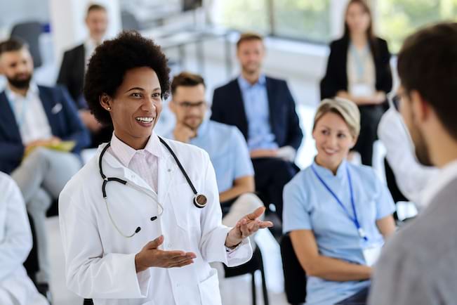 A physician standing in a class talking to another person while others look on