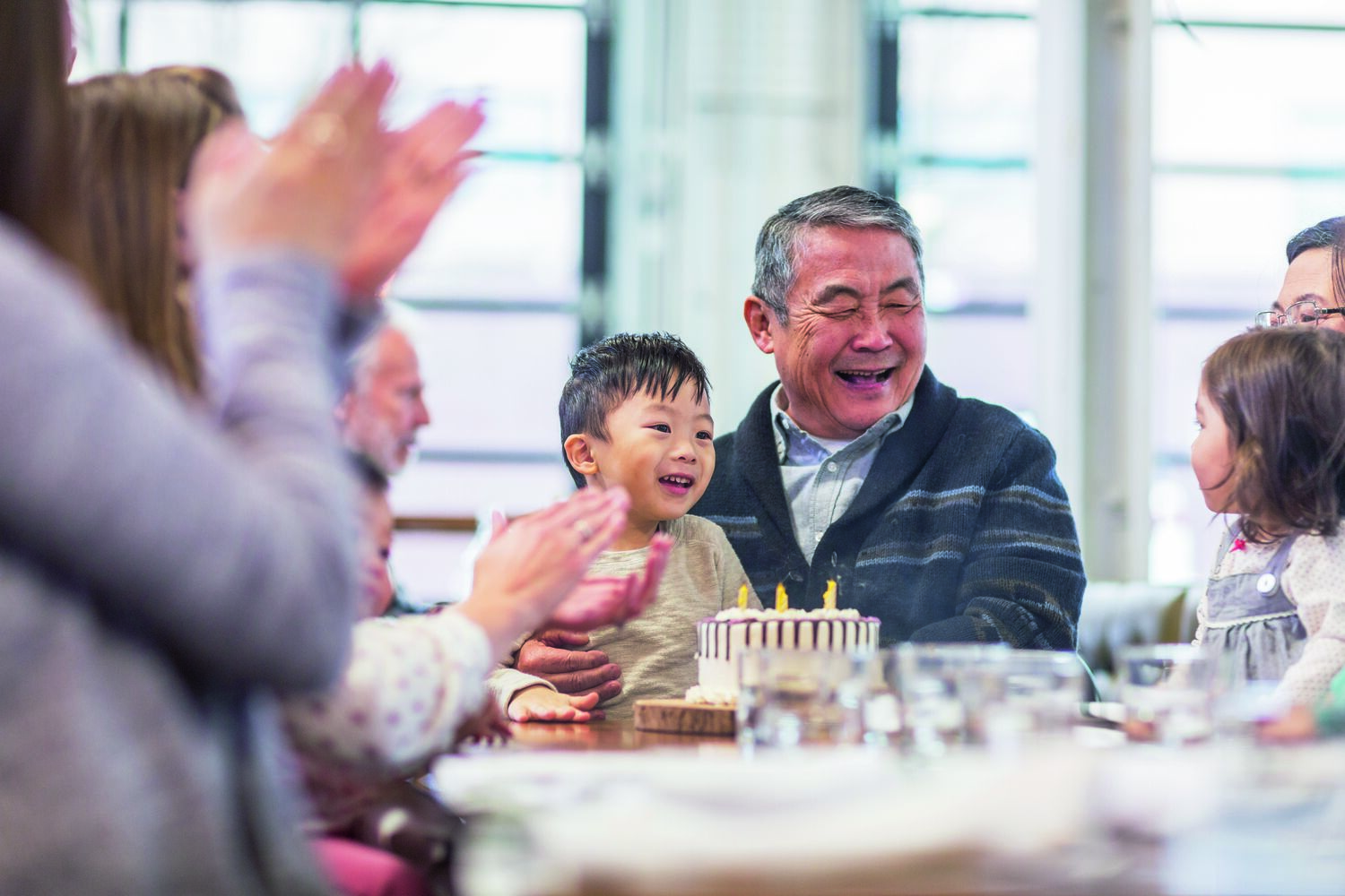 Asian father with son blowing out birthday candles on cake at party table.