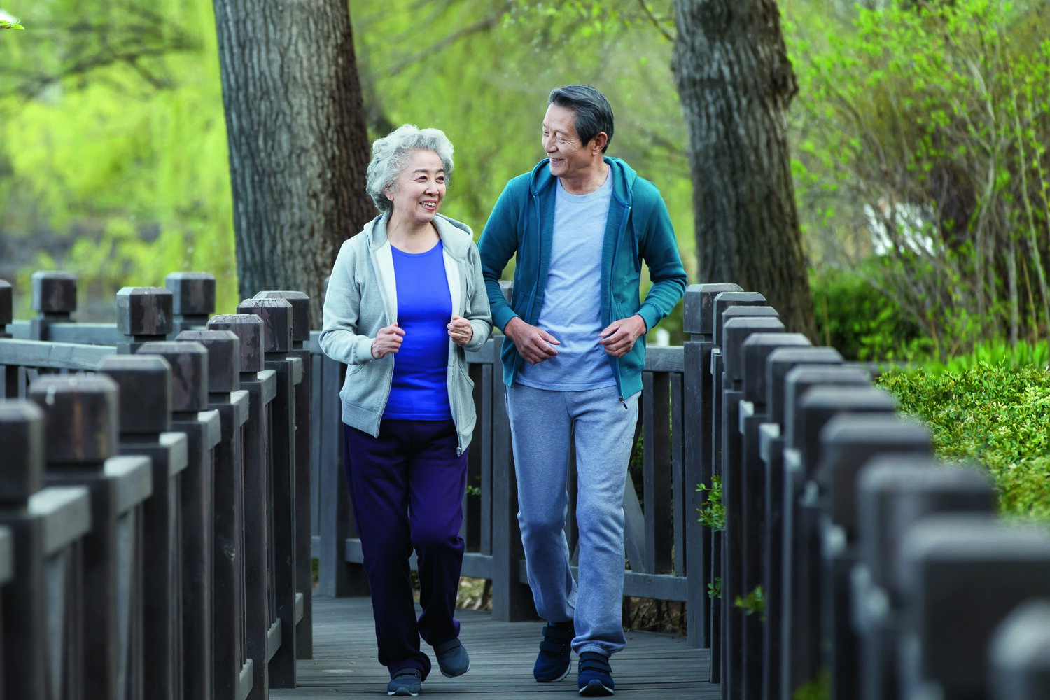 Active senior asian couple briskly walking and jogging on a bridge path outdoors.