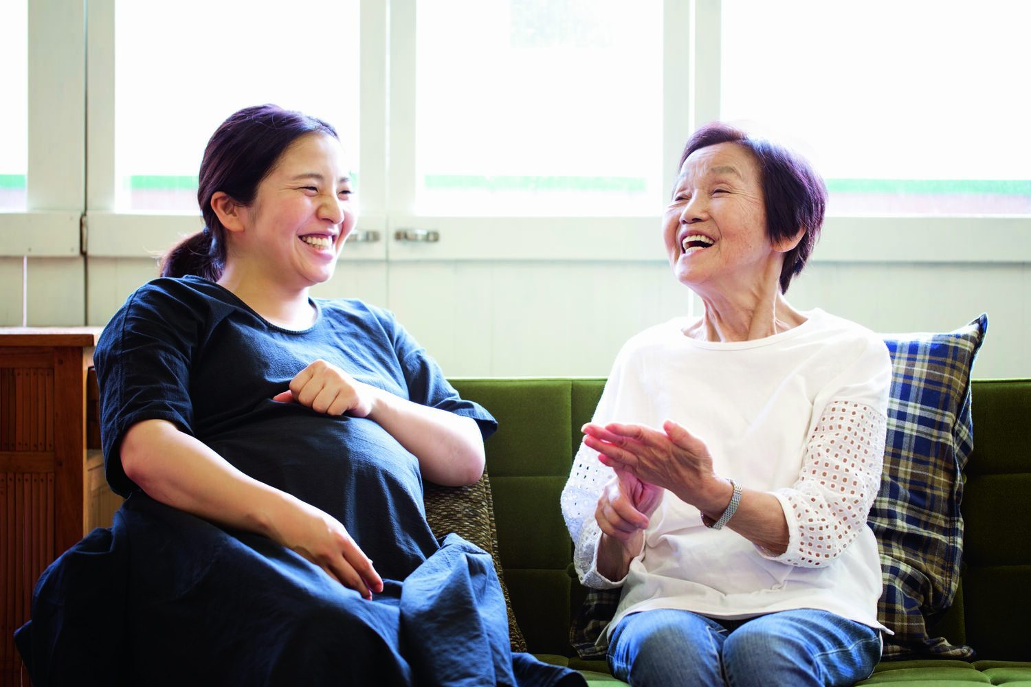 Old mother in her 80's and pregnant daughter in her 30's talking and laughing on sofa at home. Asian